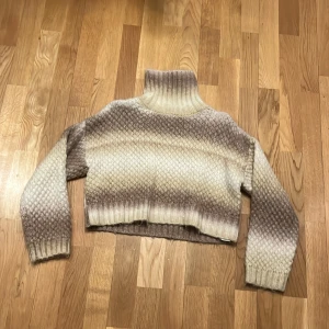 Beige och brun stickad polotröja från Zara - Säljer en mysig stickad polotröja från Zara i storlek 140. Tröjan har ett vackert ombre-mönster i beige och bruna toner. Den är croppad med långa ärmar och en hög polokrage, perfekt för kyliga dagar.❤️