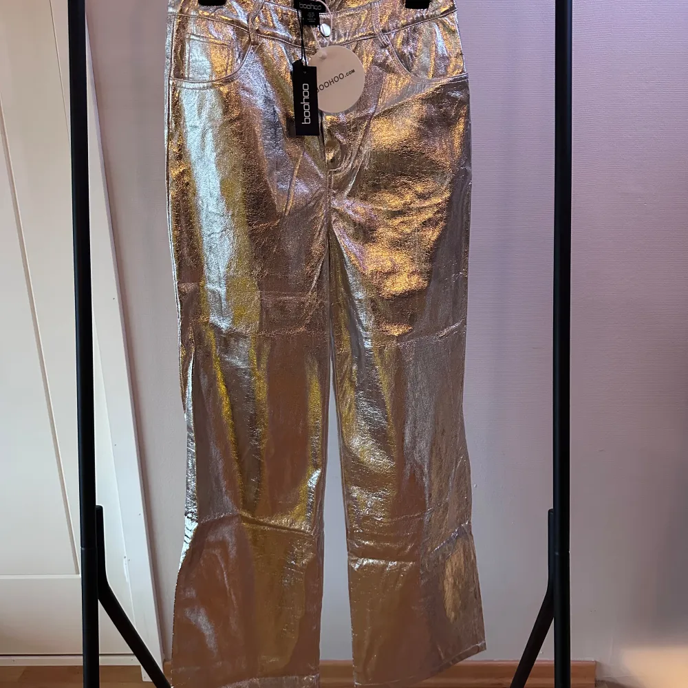 Snygga och iögonfallande silvriga byxor från Boohoo. De har en högmidjad passform och en wide stil som ger en trendig look. Perfekta för att sticka ut på festen!. Farkut & Housut.