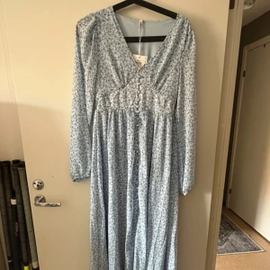 Blommig långklänning från ONLY - Säljer en vacker ljusblå långklänning från ONLY med ett fint blommönster. Klänningen har långa ärmar och en smickrande passform. Perfekt för vår och sommar!