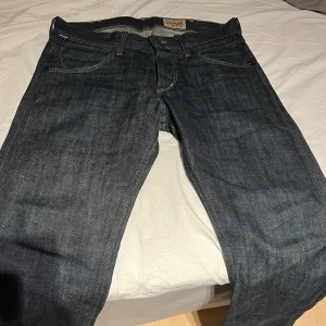 Mörkblå jeans från Wrangler - Snygga mörkblå jeans från Wrangler med klassisk femficksdesign och kontrastsömmar. Jeansen har en rak passform och är tillverkade i slitstarkt denim. Perfekta för en avslappnad stil.