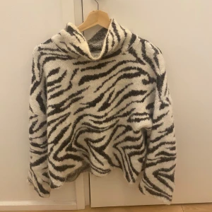 Zebramönstrad tröja med polokrage - Säljer en mysig zebramönstrad tröja med polokrage. Tröjan har en loose passform och är perfekt för kyligare dagar. Den är i svart och vit färg och har långa ärmar.