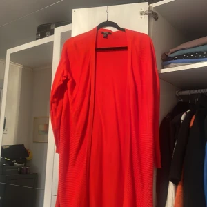 Röd långärmad kappa - Snygg röd kappa med lång ärm och öppen design. Perfekt för att lägga till en färgklick i din garderob. Passar bra till både vardag och speciella tillfällen.