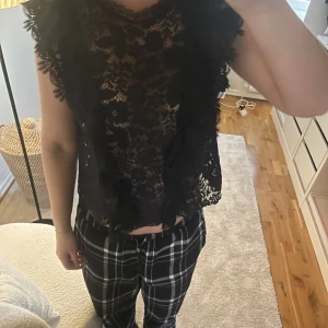 Mörkblå spetsblus - Snygg mörkblå spetsblus med volangdetaljer. Perfekt för en elegant look. Blusen är ärmlös och har ett vackert blommigt mönster Storlek M men sitter som S..