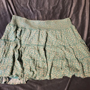 Grön blommig kjol från American Eagle - Söt grön kjol med blommigt mönster från American Eagle. Kjolen har en elastisk midja och volangdetaljer som ger en lekfull look. Perfekt för varma dagar!