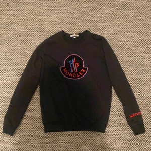 Svart sweatshirt från Moncler - Snygg svart sweatshirt från Moncler med deras ikoniska logga i rött och blått på bröstet. Tröjan har långa ärmar och Moncler-broderi på ärmen. Perfekt för en stilren look. Skick 9/10 använd 2 gånger storlek S pris 1200 pris kan diskuteras vid snabb affär 
