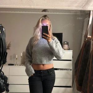 Stickad tröja - Säljer en mysig grå croppad tröja med lång ärm. Perfekt för en avslappnad stil och passar bra till jeans eller kjol. Tröjan har en enkel design som gör den lätt att matcha med andra plagg.