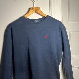Blå tröja från Ralph Lauren - Säljer en klassisk blå tröja från Ralph Lauren med det ikoniska röda broderade logotypen på bröstet. Tröjan har långa ärmar och en rund halsringning. Perfekt för en stilren och avslappnad look. Storlek 14-16 vilket motsvarar M-S, passar bra till mig som är 16/173 Nytt pris Ca:1295 mitt pris, 599-: