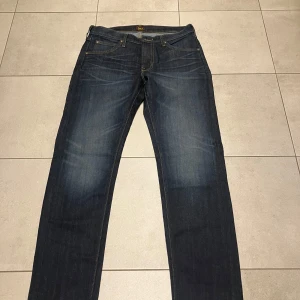 Mörkblå jeans från Lee - Snygga mörkblå jeans från Lee med dragkedja. Klassisk design med fem fickor och kontrastsömmar. Perfekta för en avslappnad stil.Oanvända jeans som vi inte fick byta i affären eftersom vi dragit bort lapparna. Från LEE i modell Daren, färg dark denim, storlek 31/30.   Nypris 1199 kr säljes för 800 kr.   Kommer från rök- och djurfritt hem. 🎄