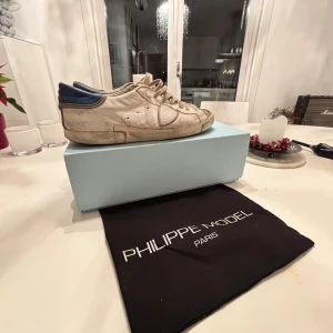 Vita sneakers från Philippe Model - Säljer ett par vita sneakers från Philippe Model med blå detaljer. Skorna har snörning och en klassisk design. Perfekta för en avslappnad stil,storlek 43 men passar också 42 och 44.Priset är inte hugget i sten!!!.