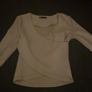 Beige omlottopp från Zara - Snygg beige omlottopp från Zara med trekvartsärm. Perfekt för en stilren look. Toppen har en v-ringad design och är gjord i ett mjukt material.