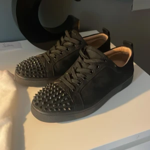Svarta sneakers med nitar från Christian Louboutin - Snygga svarta sneakers från Christian Louboutin med nitar på tån och snörning. Skorna har en stilren design med en touch av edge tack vare de dekorativa nitarna. Perfekta för att ge din outfit en unik stil.