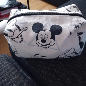 Necessär med Musse Pigg-motiv - Säljer en söt necessär med Musse Pigg-motiv. Den är vit med svarta detaljer och har en praktisk dragkedja upptill. Perfekt för att förvara smink eller andra småsaker.det finns även saker i den. 