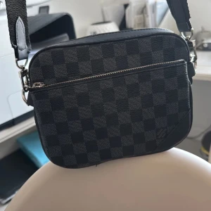 Rutig axelväska i svart och grått - Snygg axelväska med ett klassiskt rutigt mönster i svart och grått. Väskan har en praktisk dragkedja framtill och justerbar axelrem. Perfekt för att bära dina nödvändigheter med stil. Pris kan diskuteras 