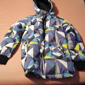 Färgglad pufferjacka med geometriskt mönster - Säljer en cool pufferjacka från Cooper i storlek 128. Jackan har ett färgglatt geometriskt mönster i blått, lila, gult och vitt. Den är utrustad med dragkedja och knappar samt en praktisk huva. Perfekt för kalla dagar!