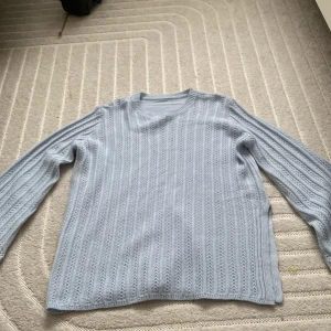 Ljusblå stickad tröja - Säljer en ljusblå stickad tröja med ett diskret mönster. Tröjan har långa ärmar och en rund halsringning. Perfekt för kyligare dagar.