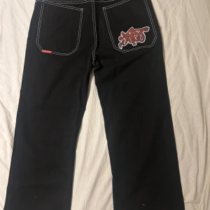 Svarta jeans - Snygga svarta jeans med kontrasterande vita sömmar och en cool röd logga på bakfickan. Byxorna har en klassisk femficksdesign och knappgylf. Perfekta för en avslappnad stil. Passar dig som är mellan 160-175 längd. Tjej och kille!