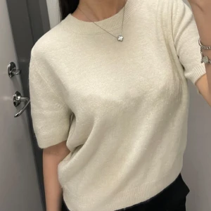Krämvit stickad tröja - Säljer en krämvit stickad tröja med korta ärmar. Perfekt för en avslappnad look och lätt att matcha med olika outfits. 