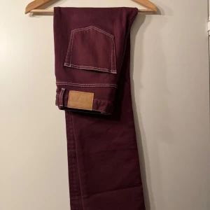Burgundy Eiffel jeans Jeanerica  - Vinröda/burgundy jeans med vita sömmar från Jeanerica i modellen Eiffel. Hög midja och lätt utsvängda nertill. Hellånga på mig som är 170cm. Knappt använda och har inga anmärkningar. Midjan är i storlek 29, men uppskattar dessa något mindre i storleken. Midjemått: 37 cm OBS produktbild i annan färg men samma modell ✨