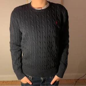 Mörkblå tröja från Ralph Lauren - Tja Säljer en stilren mörkblå kabelstickad tröja från Ralph Lauren. Tröjan har en klassisk rund halsringning och ett diskret rött broderat märke på bröstet. Perfekt för kyligare dagar. Priset kan diskuteras 