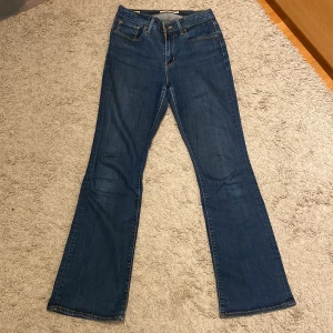 Levi's 725 High Rise Bootcut Jeans - Snygga blå Levi's 725 High Rise Bootcut jeans med klassisk femficksdesign och en bekväm hög midja. Perfekta för en avslappnad stil med en touch av retro. Tillverkade i slitstarkt denim.
