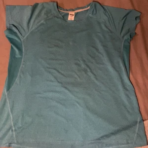 Turkos t-shirt - Säljer en turkos t-shirt i syntetmaterial. Den har korta ärmar och en rund halsringning. Perfekt för träning eller vardagsbruk.