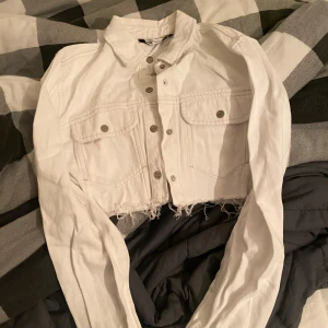 Vit croppad jacka från Zara - Säljer en snygg vit croppad jacka från Zara med knappar framtill och två bröstfickor. Jackan har långa ärmar och en stilren design som passar perfekt för vår och sommar.