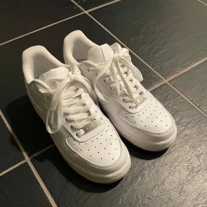 Vita Nike Air Force sneakers - Snygga och klassiska vita Nike Air Force sneakers med snörning. Perfekta för en stilren look och bekväma att bära hela dagen.