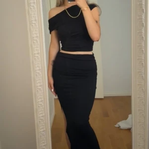 Svart offshoulder klänning - Elegant svart offshoulder klänning med tight passform. Klänningen har en stilren design och är perfekt för festliga tillfällen. Den är axelbandslös och har en lång kjol som ger en sofistikerad look.