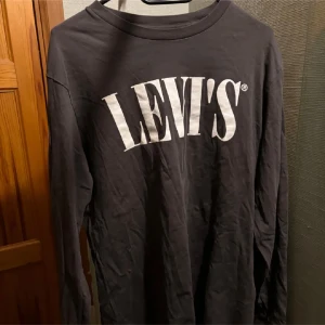 Svart långärmad tröja från Levi's - Säljer en svart långärmad tröja från Levi's med stort vitt tryck på framsidan. Tröjan har en avslappnad passform och är perfekt för en casual look. Tillverkad i mjukt material för extra komfort.