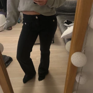 Svarta bootcut jeans - Snygga svarta bootcut jeans med låg midja. Jeansen har en dragkedja och knapp framtill. Perfekta för en stilren look. I bra skick utom slitningar nere vid hälarna, se bild.💗