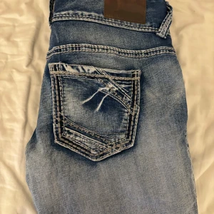 Blå jeans med broderade bakfickor - Snygga blå jeans med unika broderade detaljer på bakfickorna. De har en klassisk femficksdesign och en bekväm passform. Perfekta för en avslappnad stil.