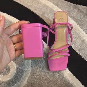 Rosa klackskor från H&M - Snygga rosa klackskor från H&M med smala remmar och fyrkantig tå. Perfekta för att ge en färgklick till din outfit. Klacken är stabil och ger bra höjd.