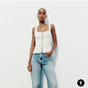 Vit ribbad korsettopp - Snygg vit ribbad korsettopp med knytning framtill. Perfekt för en stilren look. Toppen är ärmlös och har en tight passform. Den är liten i storleken!💕