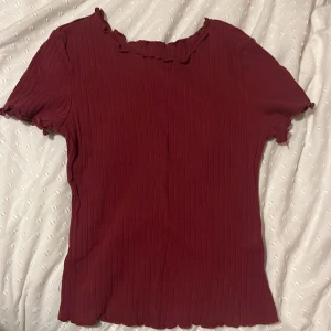 Röd ribbad topp - Säljer en röd ribbad topp med korta ärmar och volangdetaljer vid hals och ärmslut. 