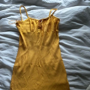 Orange ribbad klänning från Ullared - Snygg orange kortare ribbad klänning från Ullared i storlek M. Klänningen har smala axelband och en söt knytning framtill. Perfekt för varma dagar när man har en solbränna! 