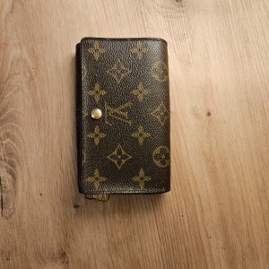 Brun plånbok  - Snygg brun plånbok med klassiskt monogrammönster. Plånboken har flera fack för kort och en knappstängning. Perfekt för att hålla ordning på dina tillhörigheter med stil. Pris går diskutera 