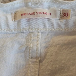 Vita Ribcage Straight jeans från Levi's - Säljer ett par vita Ribcage Straight jeans från Levi's. Dessa jeans har en hög midja och en rak passform, slitningar (som funnits från början). Ankellånga. Stl 30/32