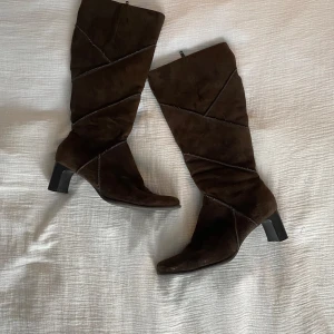 Bruna mockastövlar med klack - Snygga bruna stövlar i fuskmocka med en elegant klack och dragkedja på sidan. De har ett unikt diagonalt mönster som ger en stilren look.