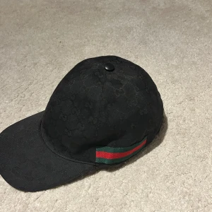 Svart keps från Gucci - Snygg svart keps från Gucci, har bara används endast en gång till ett evenemang!  Perfekt för en snygg outfit och är i ett ny skick! Kepsen ordinarie pris från Gucci för denna keps var 5000kr