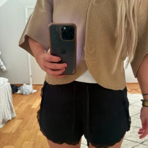 Svarta mjukisshorts med spetsdetaljer - Snygga svarta shorts med spetsdetaljer längs kanterna. Perfekta för en avslappnad stil med en touch av elegans. De har en bekväm passform och är lätta att matcha med olika toppar.