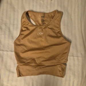 Beige sporttopp från Drop of Mindfulness - Säljer en beige sporttopp från Drop of Mindfulness. Toppen har en stilren design med brottarrygg och är tillverkad i ett mjukt och stretchigt material. Perfekt för träning eller en aktiv vardag.