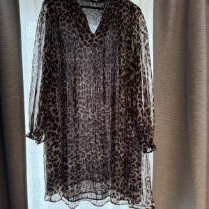 Leopardmönstrad klänning från Mango - Trendig leopardmönstrad klänning från Mango med v-ringning och långa ärmar. Klänningen har en luftig passform och är perfekt för att ge en djärv look. Tillverkad i ett lätt och bekvämt material.