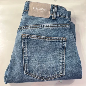 Blå jeans från Pull&Bear - Blå jeans från Pull&Bear med slitna detaljer på knäna. Raka ben med lite bootcut och slits längst ner. Jeansen är i storlek 32 och är i bra skick 