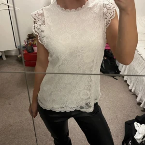 Vit spetsblus - Säljer en elegant vit spetsblus med vackra detaljer. Blusen har korta ärmar med volang och ett fint mönster. Perfekt för en stilren look.