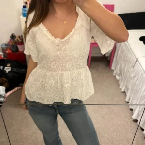 Vit blus med spetsdetaljer - Säljer en söt vit blus med spetsdetaljer och v-ringad hals. Blusen har korta ärmar och ett fint broderat mönster. Perfekt för en somrig look!