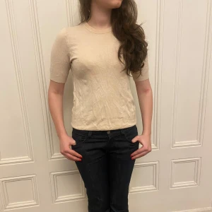 Beige kortärmad topp med knappar - Säljer en stilren beige topp med korta ärmar och rund hals. Toppen har knappar i ryggen som ger en extra detalj. Perfekt för en avslappnad men ändå fin look!