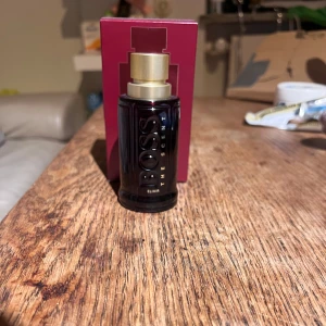 BOSS The Scent Elixir Parfym - Elegant parfymflaska från BOSS i en djup mörkröd nyans med en stilren guldfärgad kork. 50 ml. Flaskan har en lyxig och modern design, perfekt för den som vill ha en sofistikerad doftupplevelse. Nypris ligger på 1300 kr. Använt cirka 5 ml. Säljer gör 600 kr