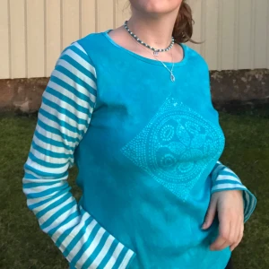 Turkos långärmad tröja med randiga ärmar - Säljer en cool turkos tröja med ett unikt mönster på framsidan. Den har randiga ärmar i turkos och vitt som ger en snygg kontrast. Perfekt för en avslappnad stil och passar bra till både jeans och kjol. Tröjan är i bra skick och redo för nya äventyr!