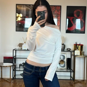Vit off-shoulder topp 💓 - Säljer en superfin vit off-shoulder topp som är perfekt för både vardag och fest. Den är långärmad och har en tight passform som framhäver figuren. Materialet känns mjukt och stretchigt, vilket gör den bekväm att bära hela dagen. Toppen är stilren och kan enkelt matchas med både jeans och kjol.