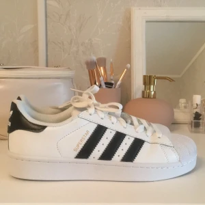Adidas Superstar sneakers - Säljer ett par klassiska Adidas Superstar sneakers i vitt med svarta detaljer. Helt oanvända och i superbra skick! Säljer för att jag inte passade dem så bra och säkert passar någon annan bättre.☺️